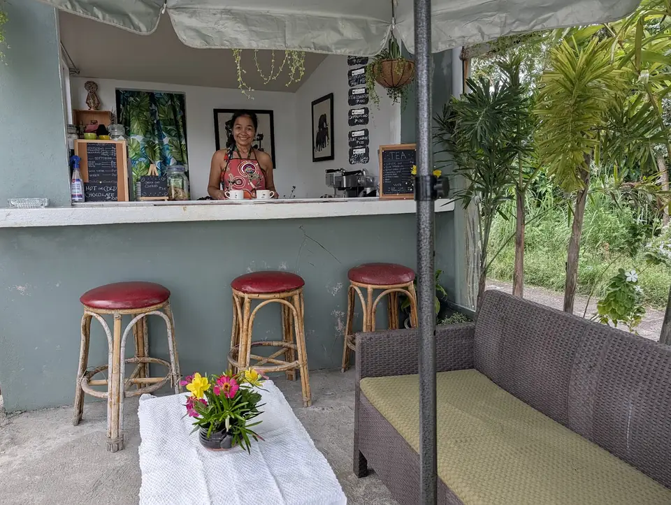 Kape Parola's smiling proprietor behind the open counter, with rattan stools and garden seating
