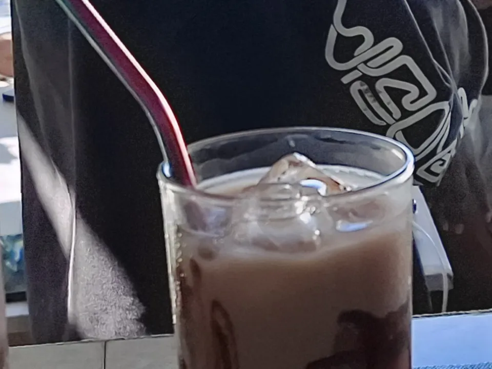 A row of tall iced chocolate drinks on the Kape Parola counter with the sea view behind
