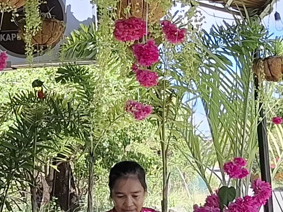 Jackie, the owner of Kape Parola, at the cafe's long table beneath hanging plants and bougainvillea